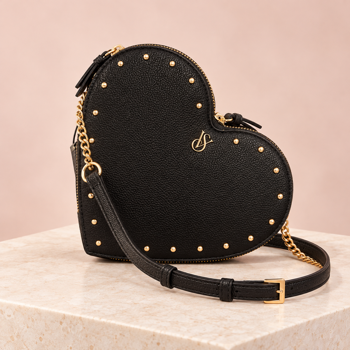 Cartera corazón Victoria’s Secret negra con tachas doradas en el borde y correa larga.