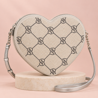Cartera corazón Victoria’s Secret plateada con monograma VS y correa larga, vista frontal.