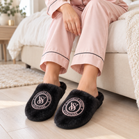 Mujer en pijama usando pantuflas Victoria’s Secret negras con bordado rosado
